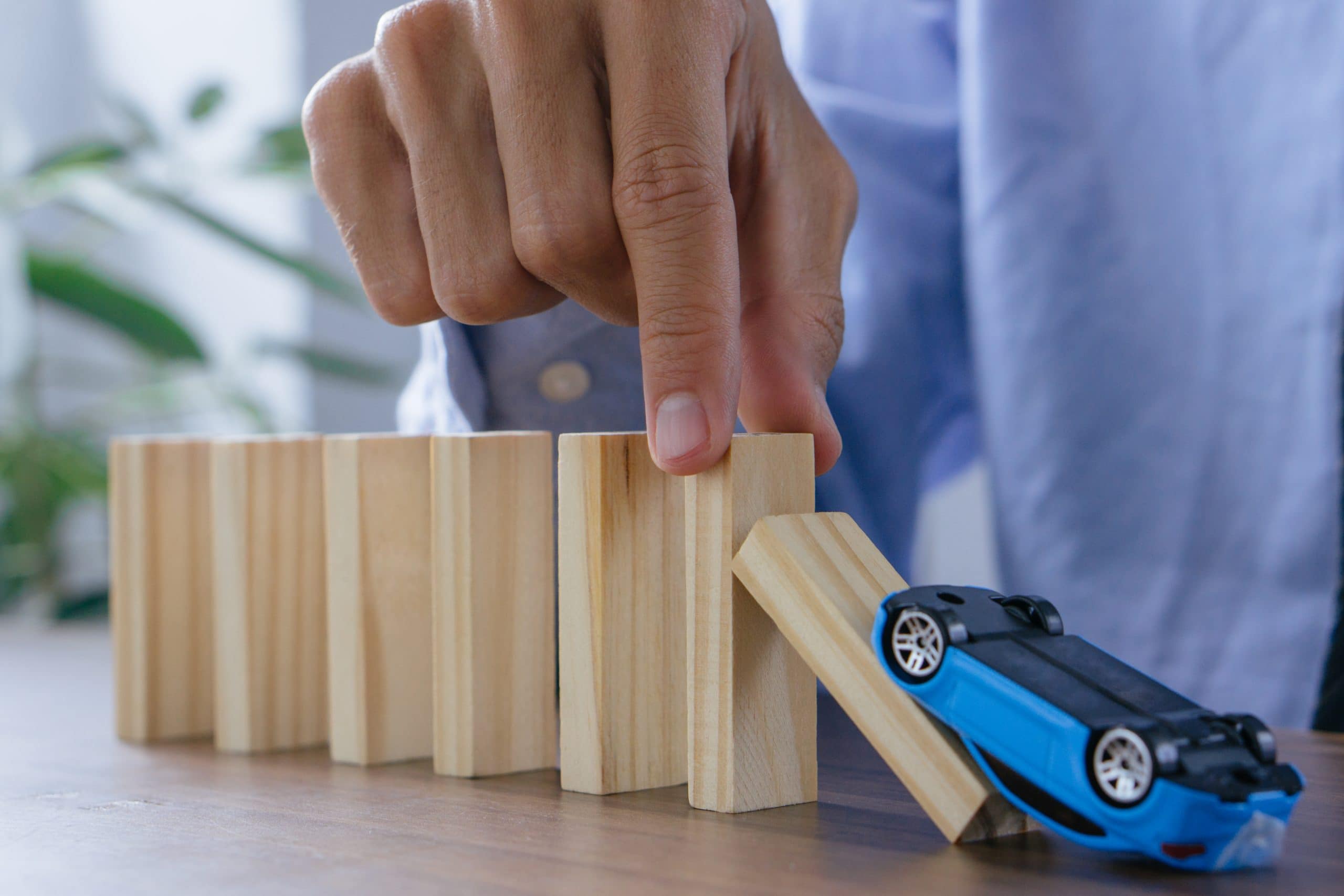 A hand prevents falling wooden blocks as a blue toy car flips, symbolizing Umbrella Excess Liability.