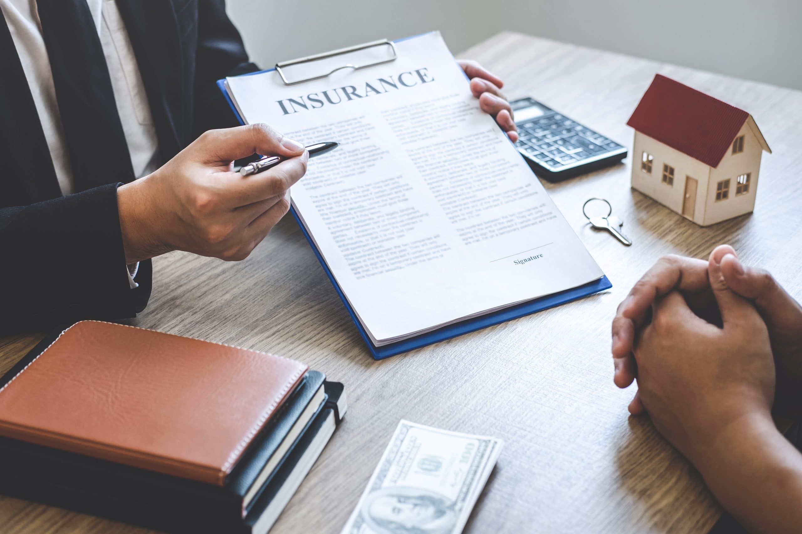 Two people review a manufactured home insurance contract at a desk with cash, house model, and calculator.
