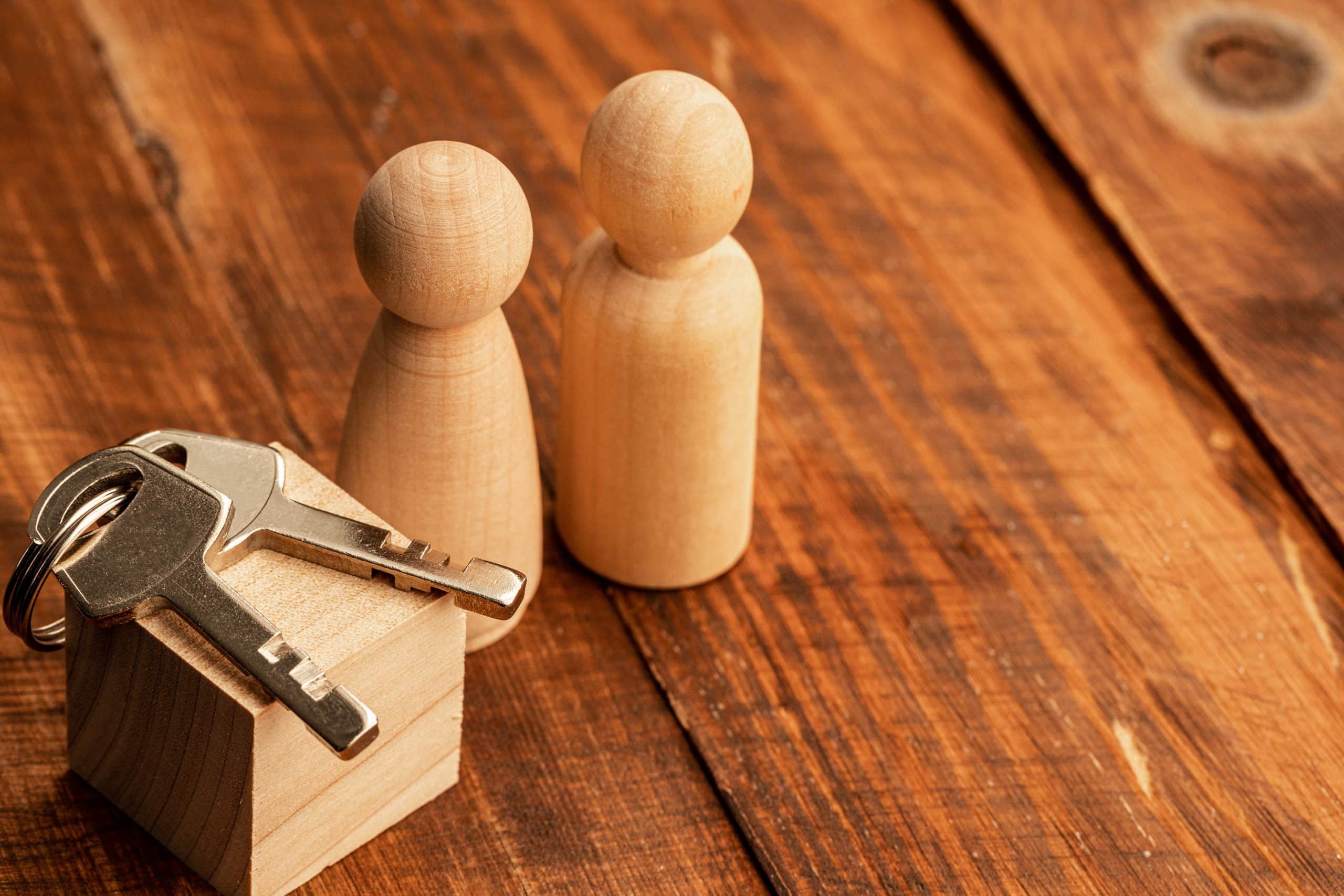Two wood figures and a small house block with keys on top represent landlord insurance on rustic wood.