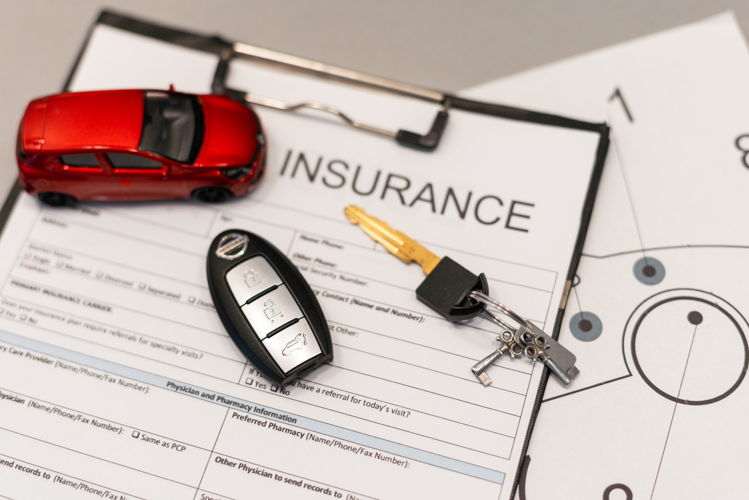 Red toy car, car key, and remote rest on rental car insurance documents with a clipboard in the background.