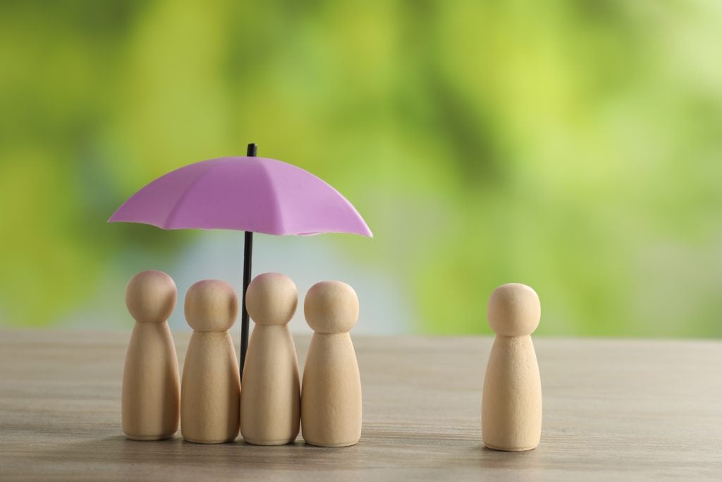 Five wooden figures stand under a purple umbrella showing umbrella coverage; one stands alone nearby.