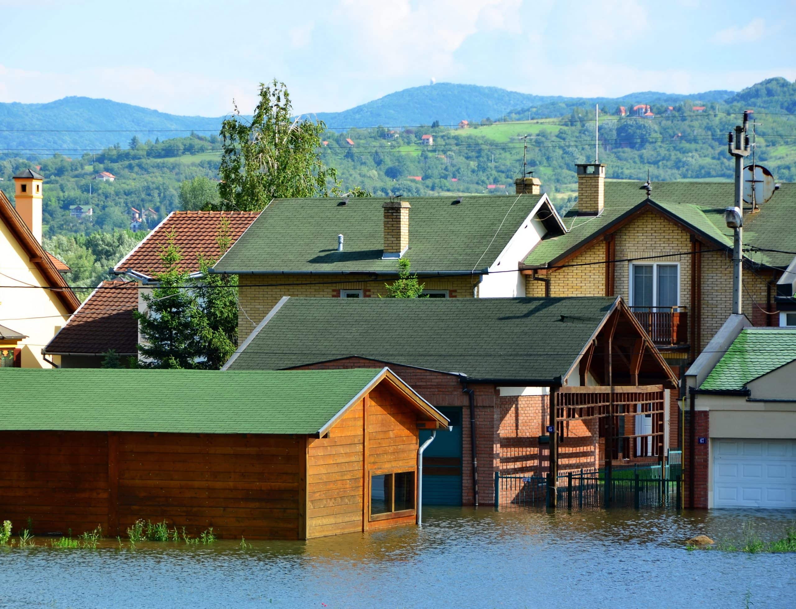 Floodwaters submerge houses and garages in a residential area with hills visible in the background.