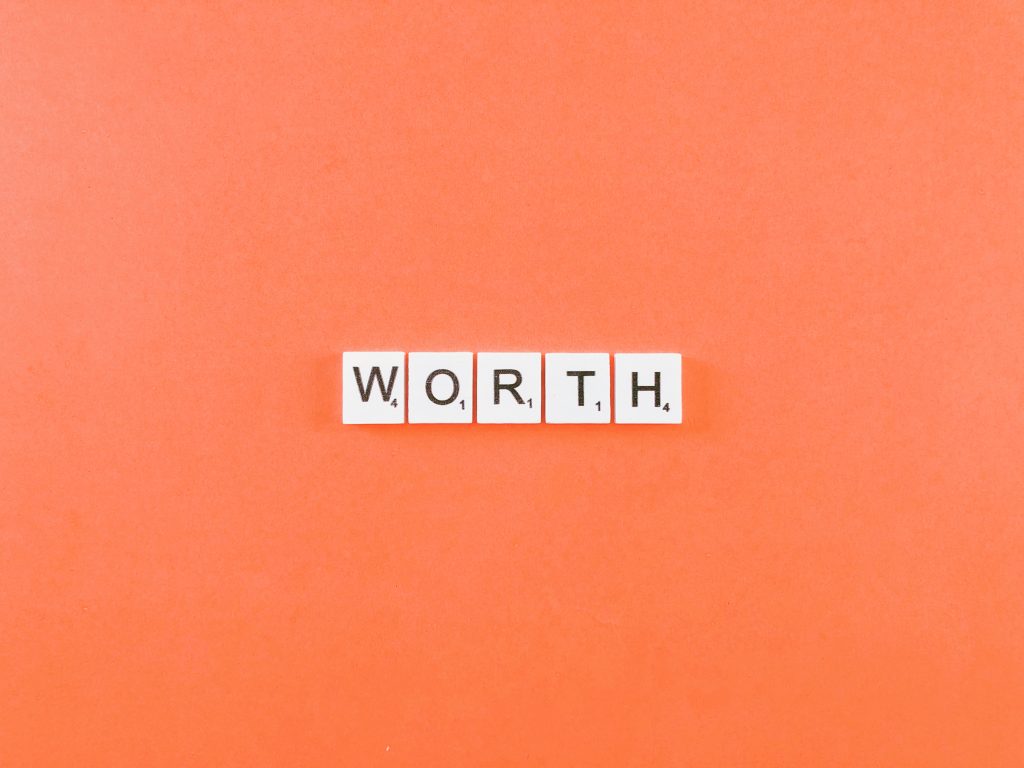 White tiles spelling “WORTH” are arranged on an orange background, emphasizing value in bold letters.