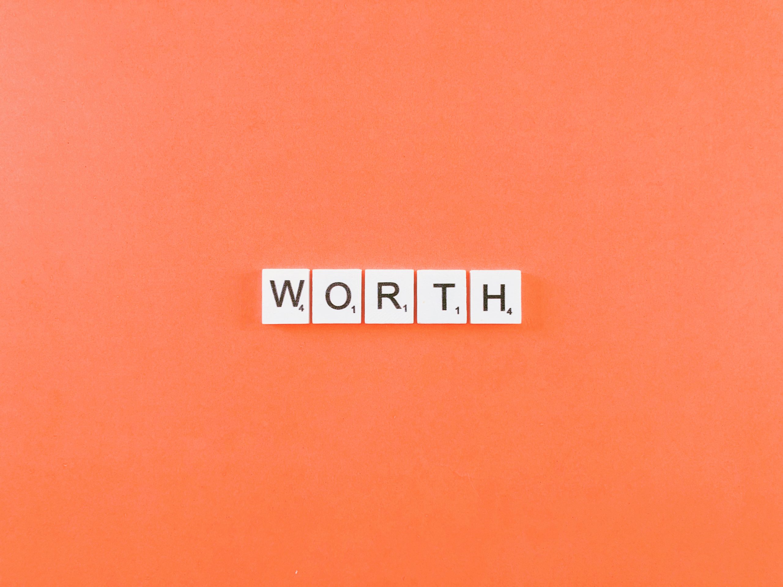 White tiles spelling “WORTH” are arranged on an orange background, emphasizing value in bold letters.