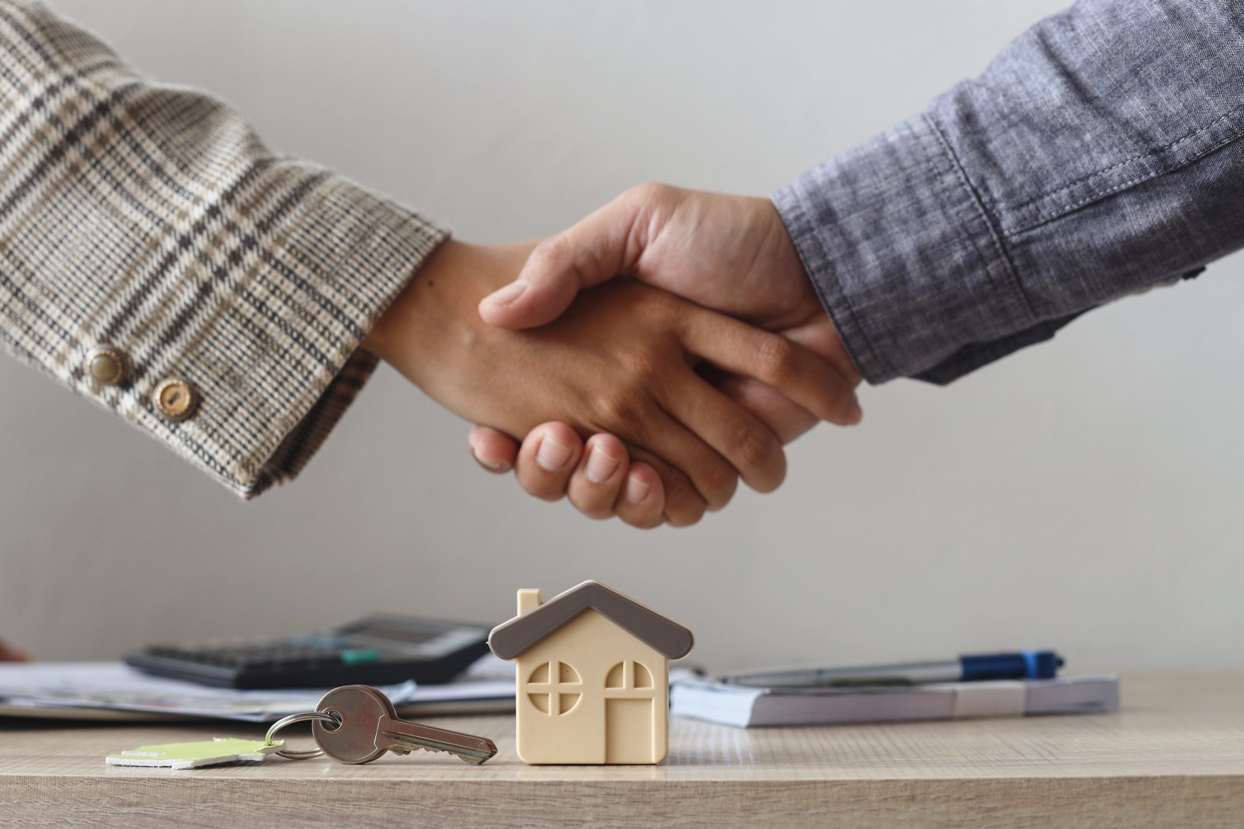 Two people shake hands by a small house model and keys, illustrating a successful property deal.