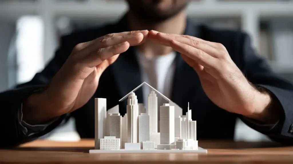 Hands form a roof shape over a model city, highlighting protection and insurance for urban buildings.
