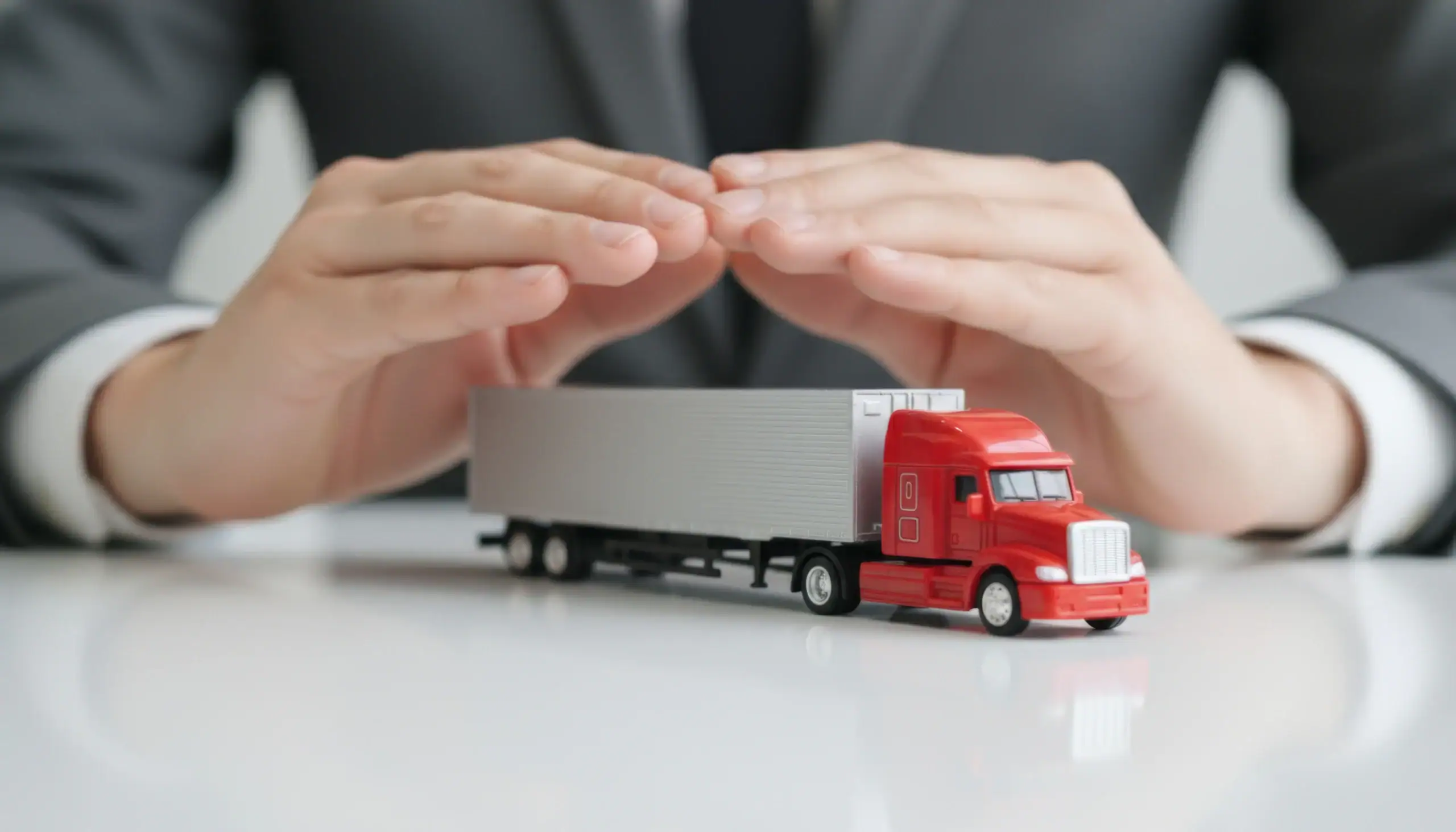 Hands hover protectively over a red toy truck, showing vehicle insurance or transport protection.