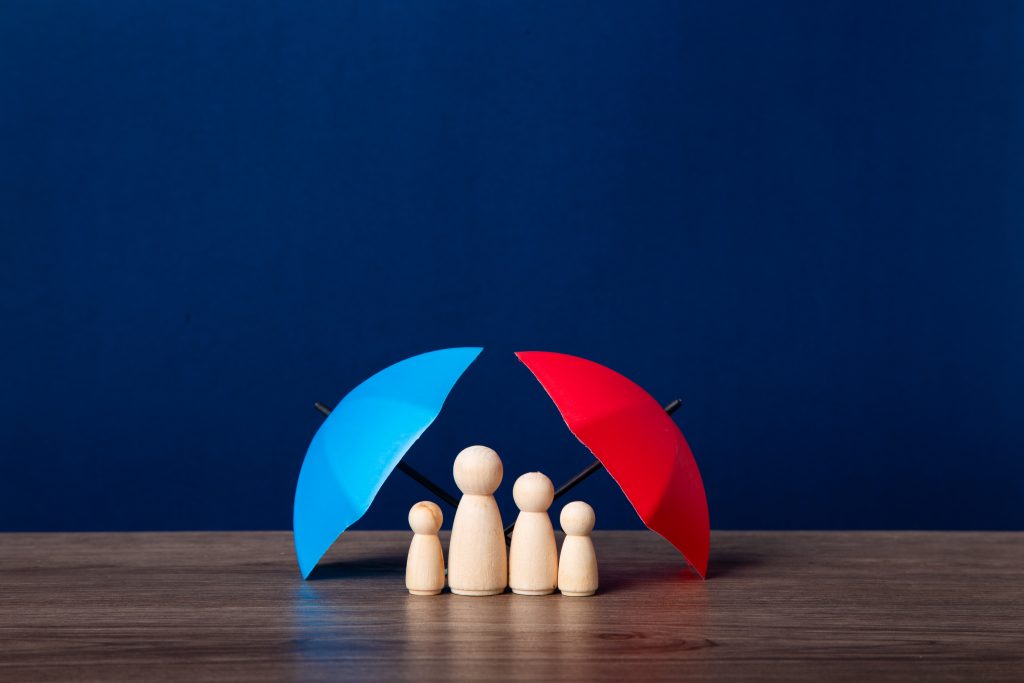 Four wooden figures stand under blue and red umbrellas on a wooden surface with a blue background.